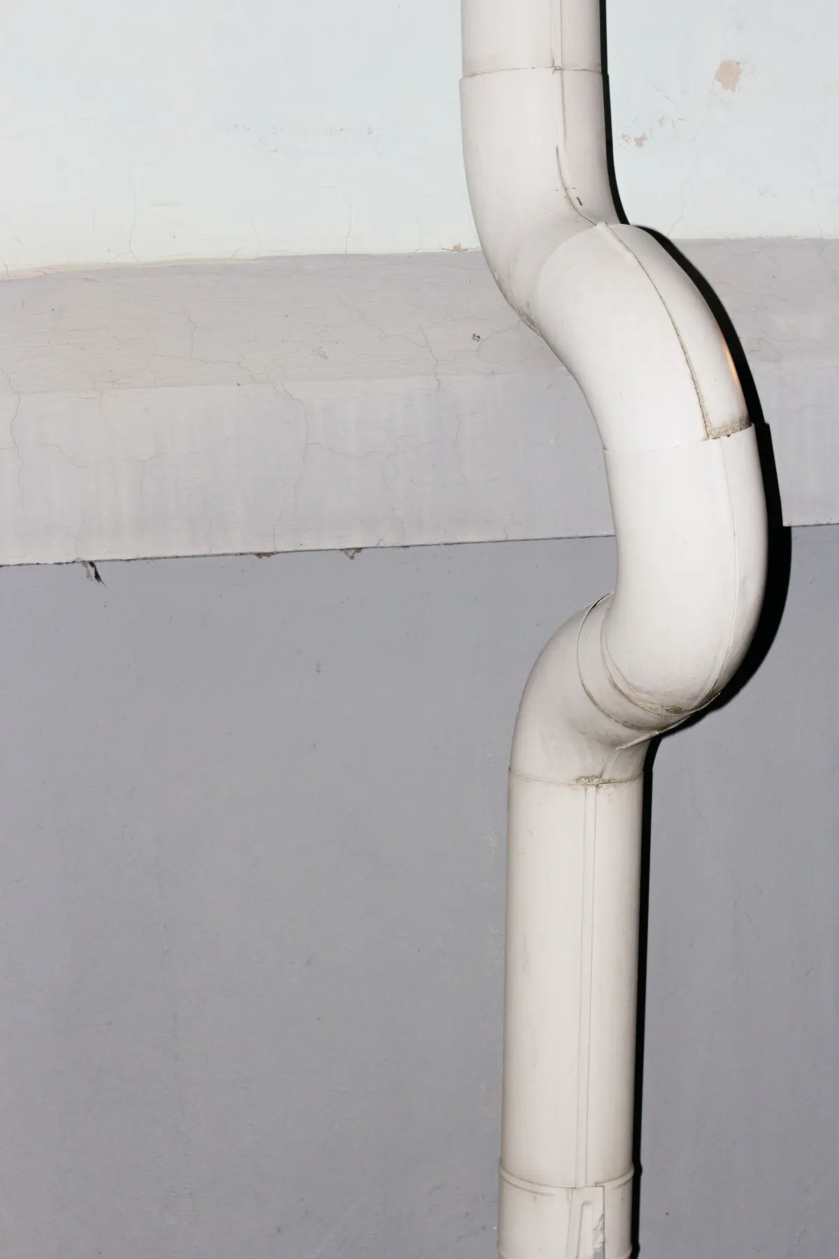 Caño de desagüe blanco con curva instalado sobre una pared de hormigón